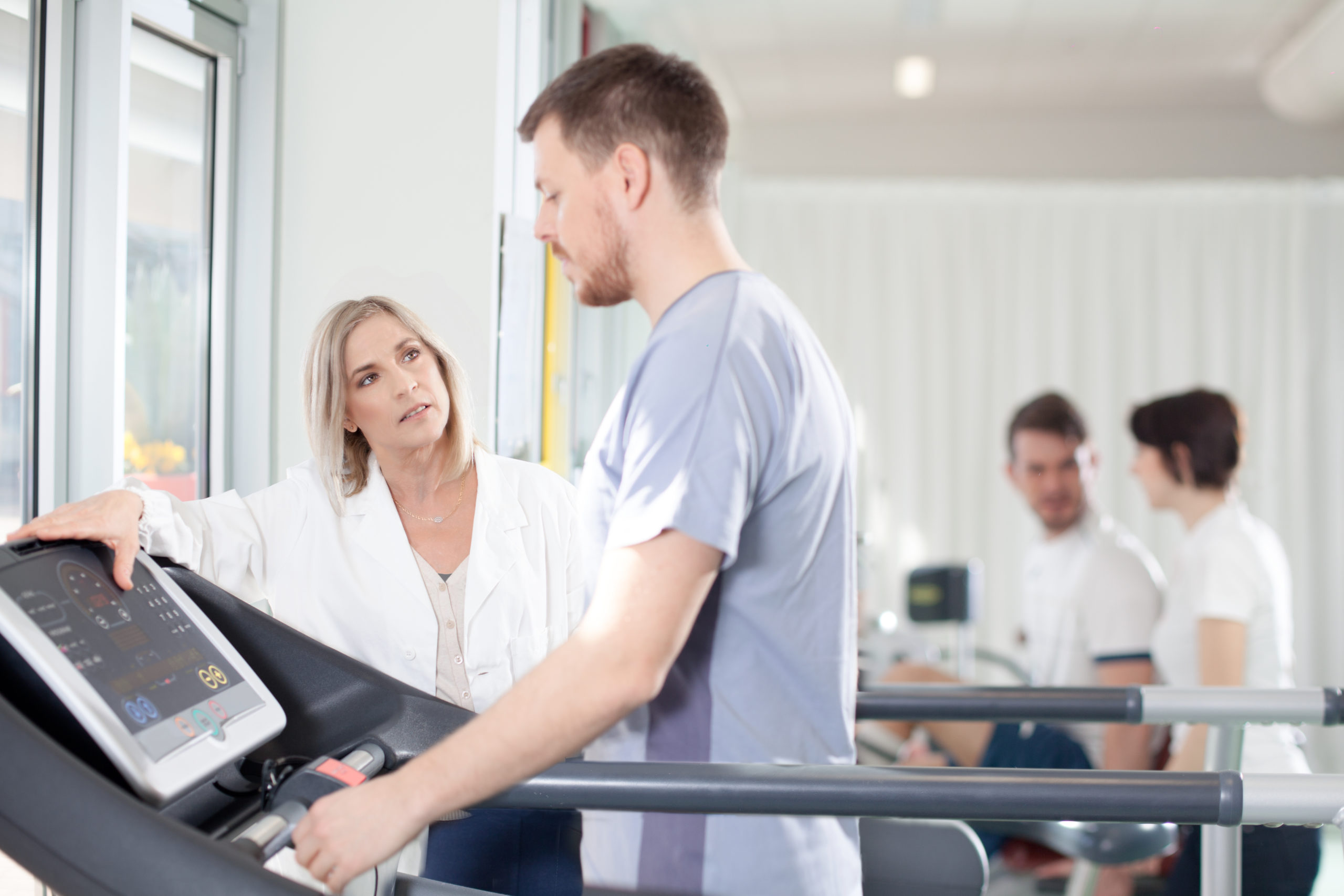 athlete on a treadmill with physiotherapist doctor athlete on the treadmill he performs the instructions of physical therapist who assists him. in the background other athletes